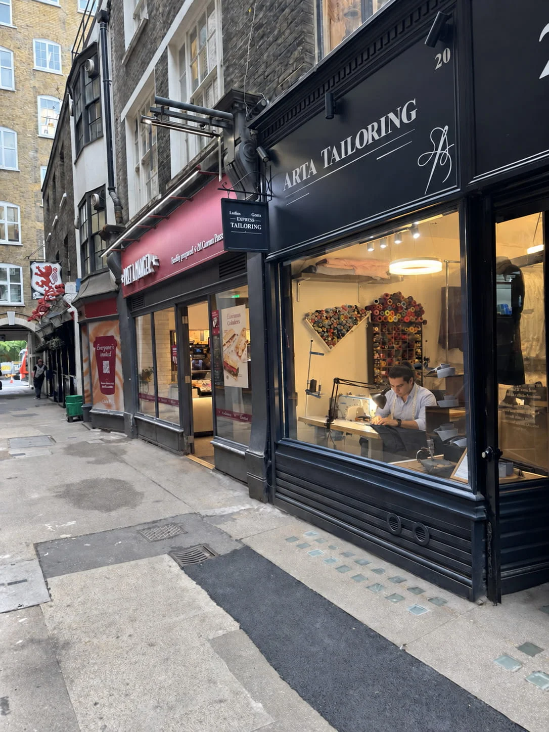 Arta Tailoring shopfront at 20 Crown Passage in St James's London with master tailor sewing in window